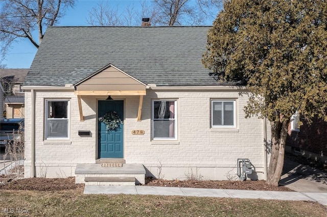 view of front of home featuring a shingled roof, a chimney, and brick siding