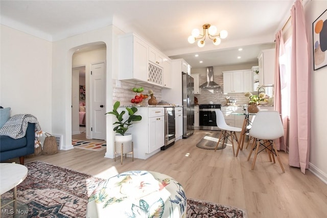 interior space featuring light wood finished floors, arched walkways, range, wall chimney exhaust hood, and freestanding refrigerator