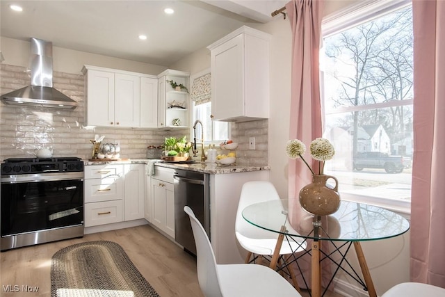 kitchen featuring dishwasher, gas range oven, wall chimney range hood, white cabinetry, and open shelves