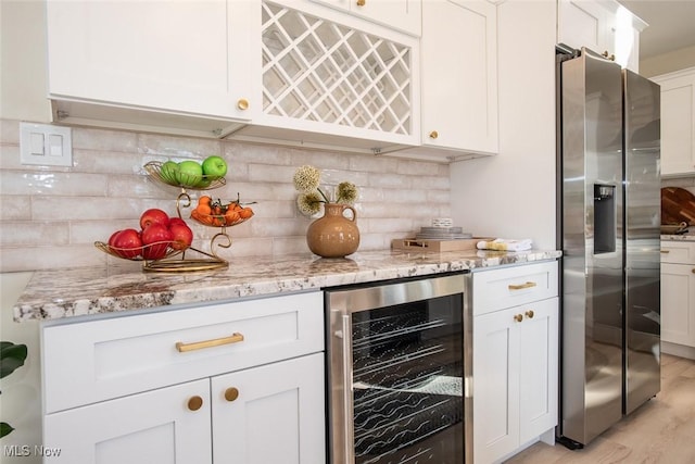 bar with a dry bar, tasteful backsplash, beverage cooler, light wood-style flooring, and stainless steel refrigerator with ice dispenser