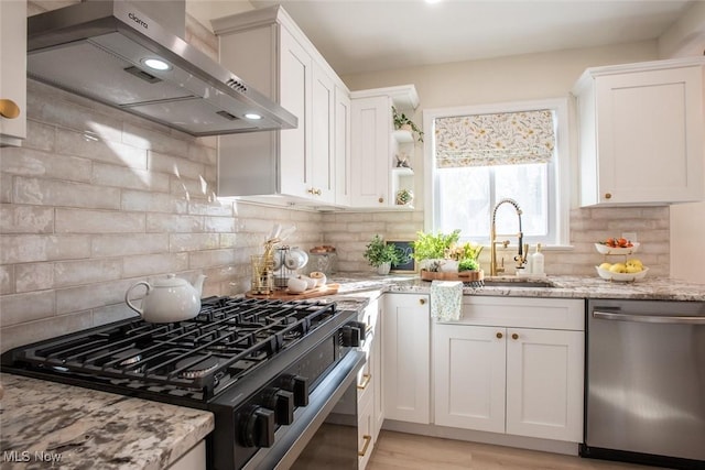 kitchen featuring stainless steel dishwasher, wall chimney range hood, white cabinetry, a sink, and gas stove