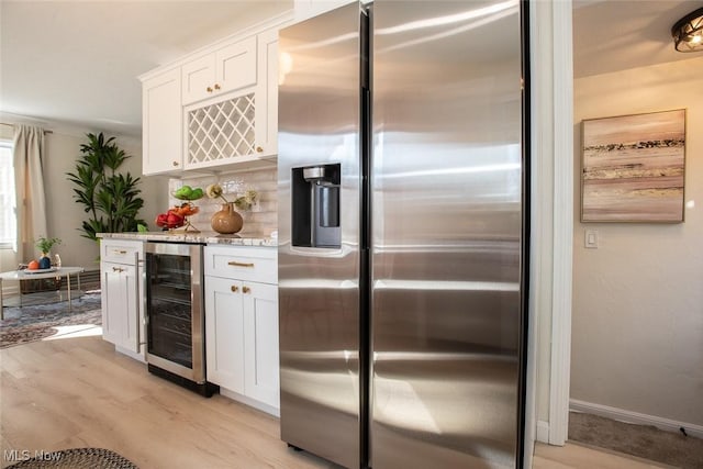 kitchen featuring light wood-style flooring, white cabinetry, light stone countertops, beverage cooler, and stainless steel fridge