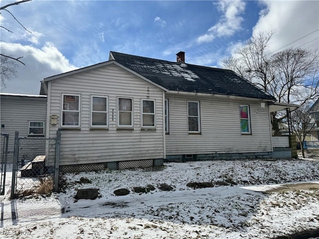 snow covered property with a shingled roof, a chimney, and fence