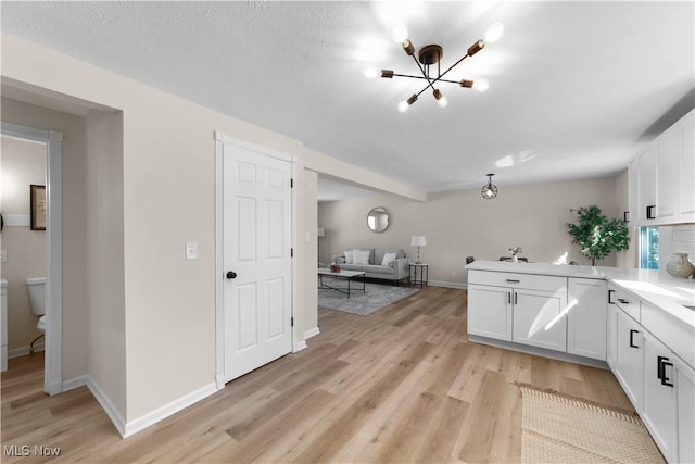 kitchen featuring light countertops, light wood-style flooring, white cabinets, a peninsula, and baseboards