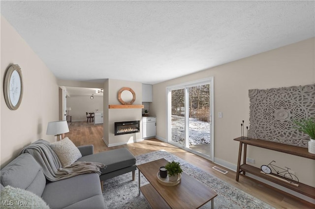 living area with light wood-style floors, visible vents, a textured ceiling, and a glass covered fireplace