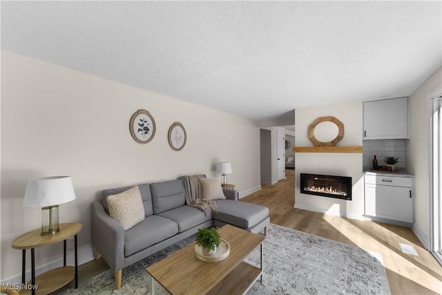 living room with light wood-style floors, a glass covered fireplace, and baseboards