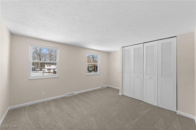 unfurnished bedroom featuring baseboards, visible vents, a textured ceiling, carpet flooring, and a closet