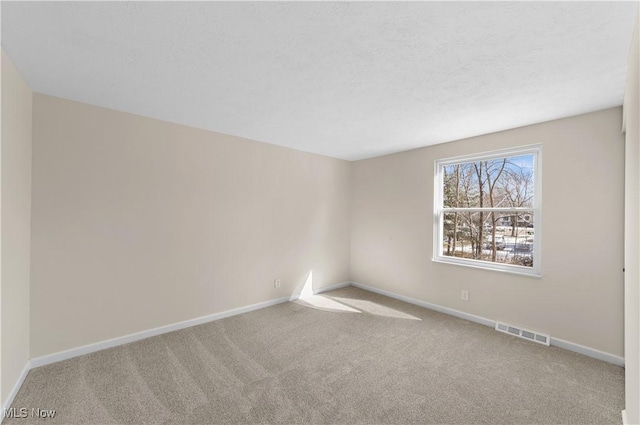 carpeted spare room featuring visible vents, a textured ceiling, and baseboards