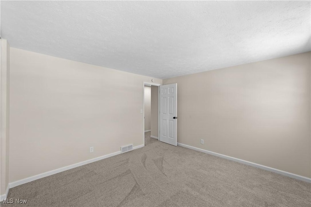 spare room with carpet floors, visible vents, a textured ceiling, and baseboards