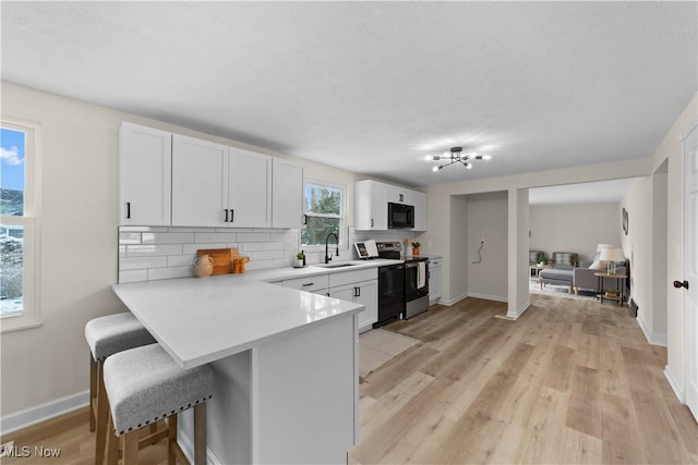 kitchen with black microwave, a sink, a kitchen breakfast bar, light countertops, and stainless steel electric range