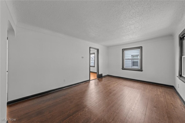 spare room featuring a textured ceiling, wood-type flooring, and baseboards