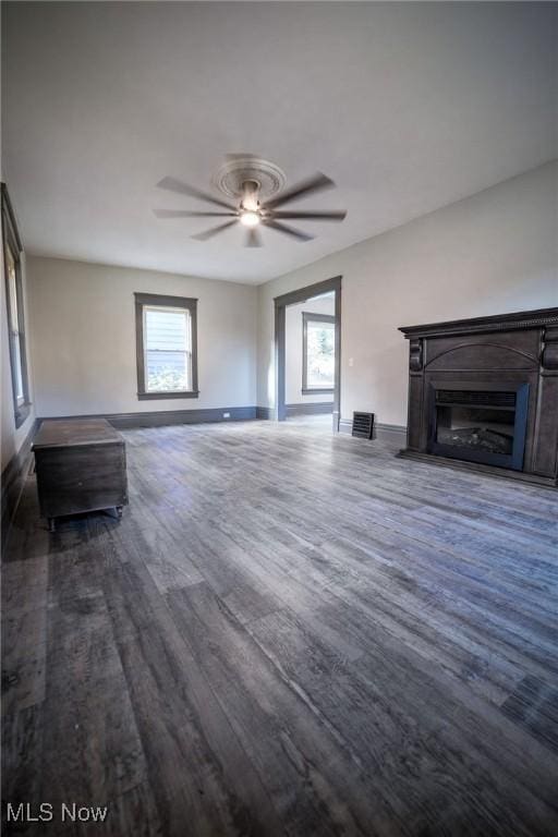 unfurnished living room featuring dark wood finished floors, a fireplace, baseboards, and ceiling fan