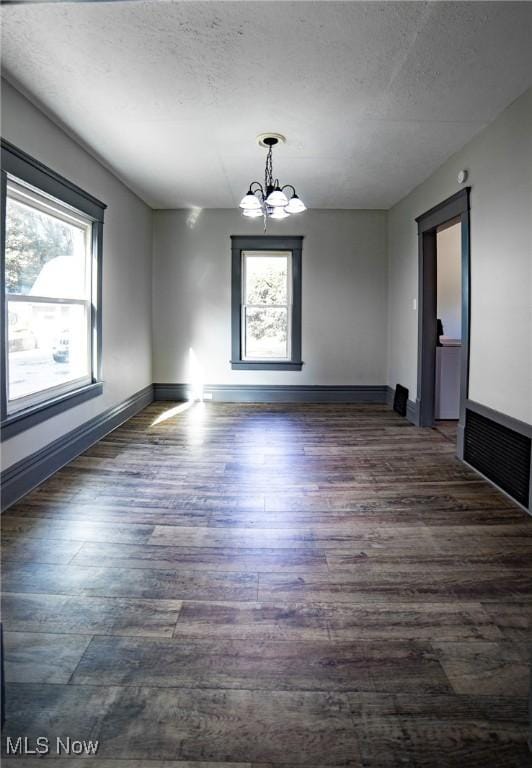 unfurnished room featuring visible vents, baseboards, wood finished floors, a notable chandelier, and a textured ceiling