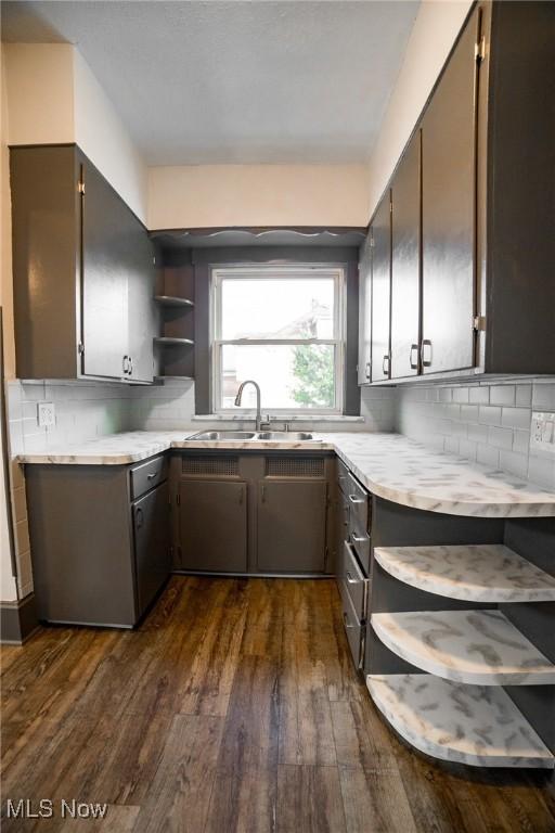 kitchen featuring open shelves, a sink, tasteful backsplash, light countertops, and dark wood-style flooring