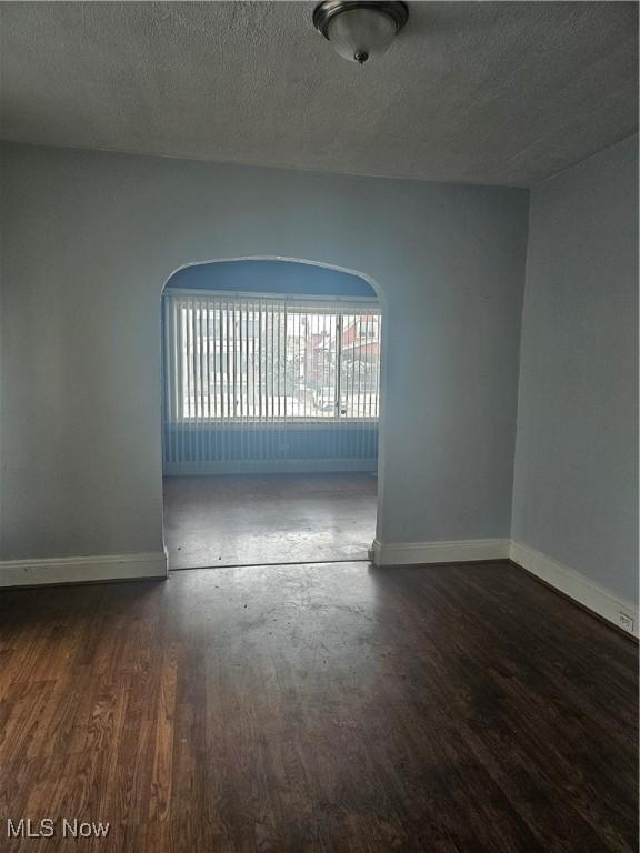 empty room with baseboards, a textured ceiling, and wood finished floors