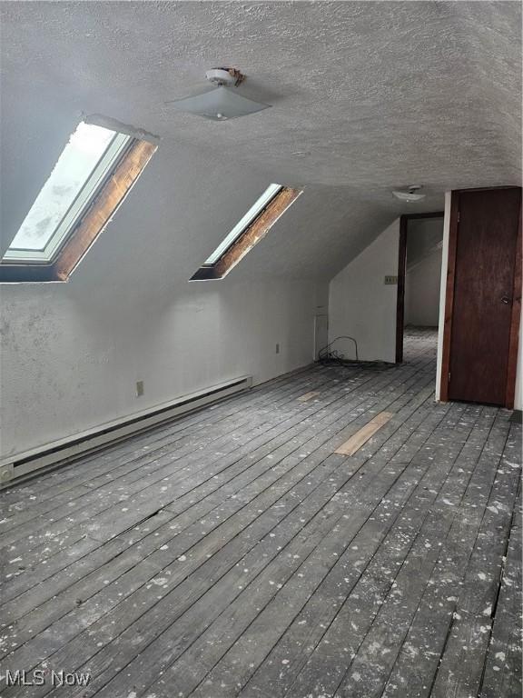 bonus room with a baseboard radiator, vaulted ceiling with skylight, a textured ceiling, and hardwood / wood-style floors