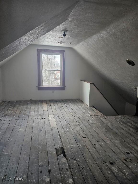 additional living space featuring hardwood / wood-style floors, vaulted ceiling, and a textured ceiling