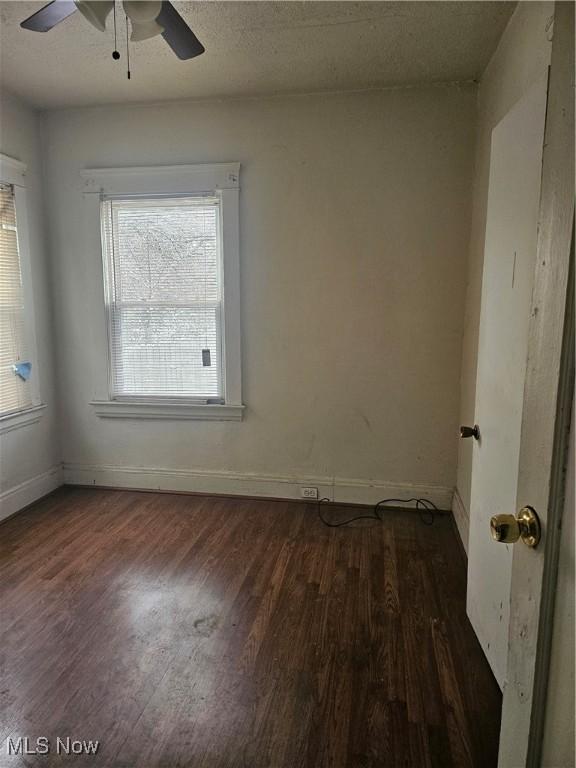 empty room with a textured ceiling, wood finished floors, baseboards, and ceiling fan