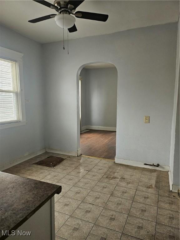 empty room with arched walkways, ceiling fan, and baseboards