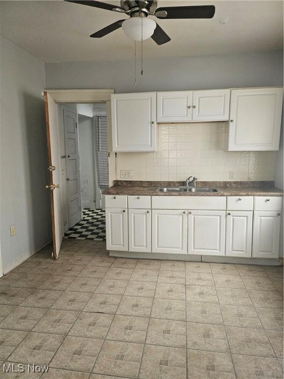 kitchen with white cabinetry, dark countertops, decorative backsplash, and a sink