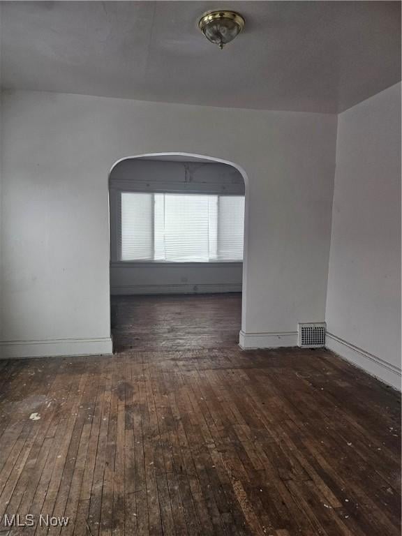 unfurnished room with arched walkways, visible vents, baseboards, and hardwood / wood-style flooring