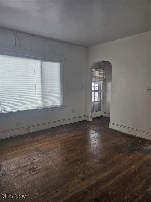 unfurnished room featuring baseboards, arched walkways, and dark wood finished floors