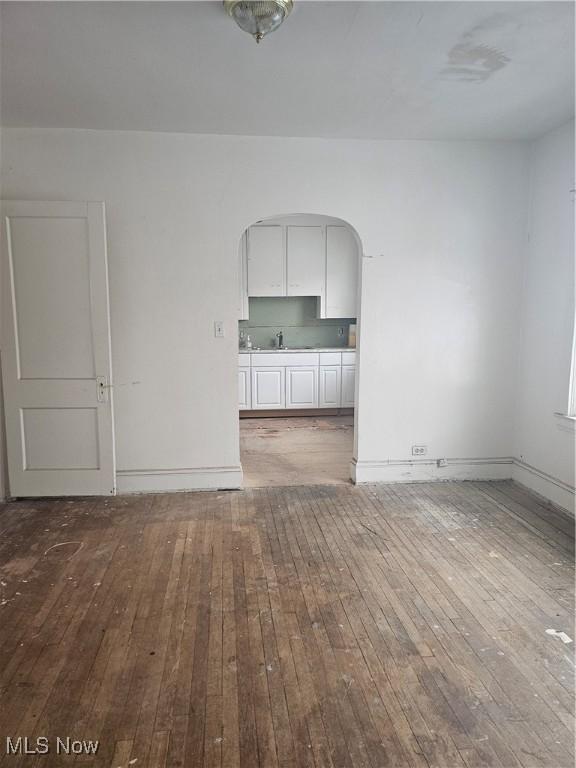 unfurnished living room featuring a sink, baseboards, arched walkways, and wood-type flooring