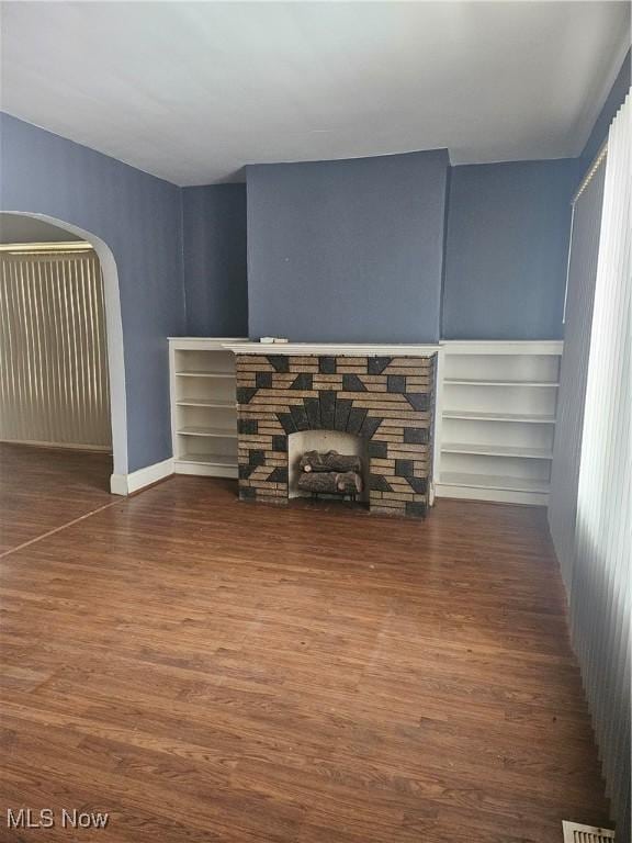 unfurnished living room featuring a stone fireplace, wood finished floors, and arched walkways