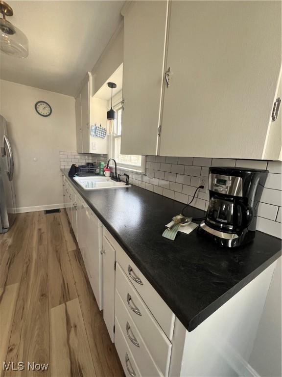 kitchen with dark countertops, decorative backsplash, light wood-style floors, white cabinets, and a sink