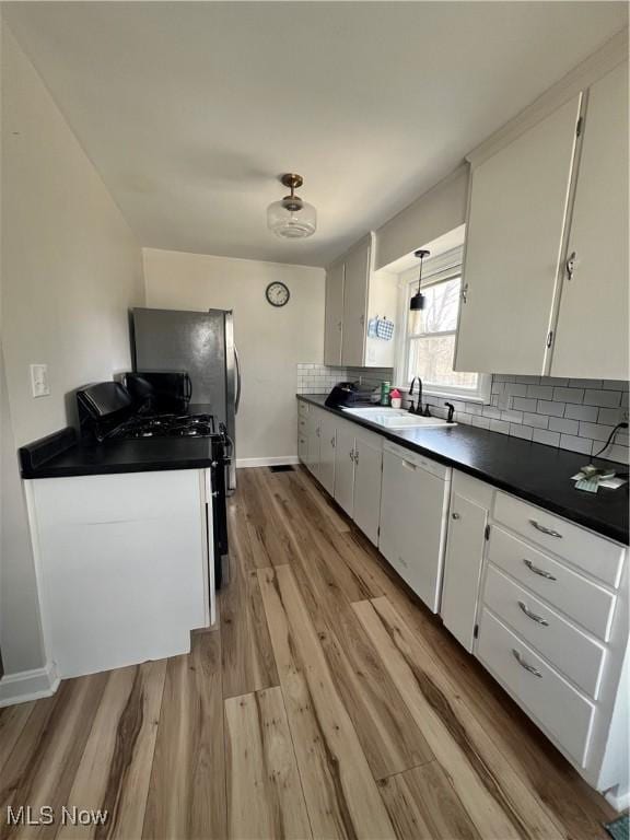 kitchen featuring dark countertops, backsplash, white cabinets, a sink, and light wood-type flooring