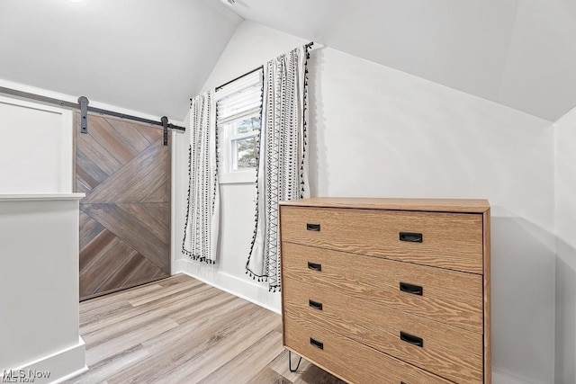 interior space with vaulted ceiling, light wood finished floors, and a barn door