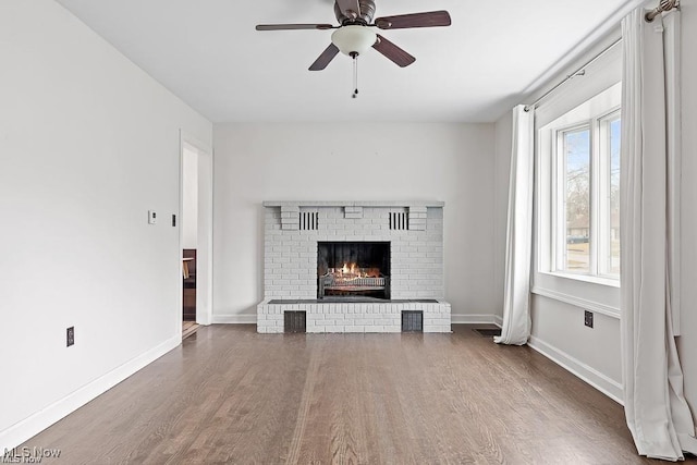 unfurnished living room with a brick fireplace, a ceiling fan, baseboards, and wood finished floors