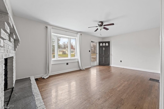 unfurnished living room with baseboards, visible vents, dark wood-style floors, ceiling fan, and a fireplace