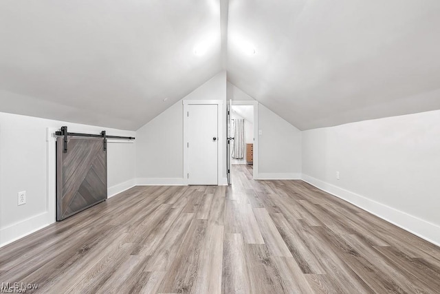 additional living space with lofted ceiling, a barn door, wood finished floors, and baseboards