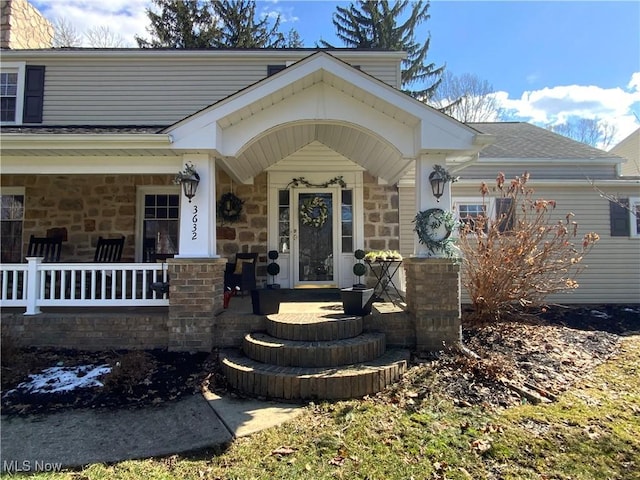 view of exterior entry with covered porch, stone siding, and roof with shingles