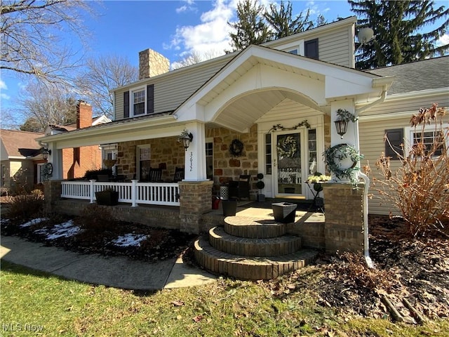 view of front facade featuring a porch, stone siding, and a chimney