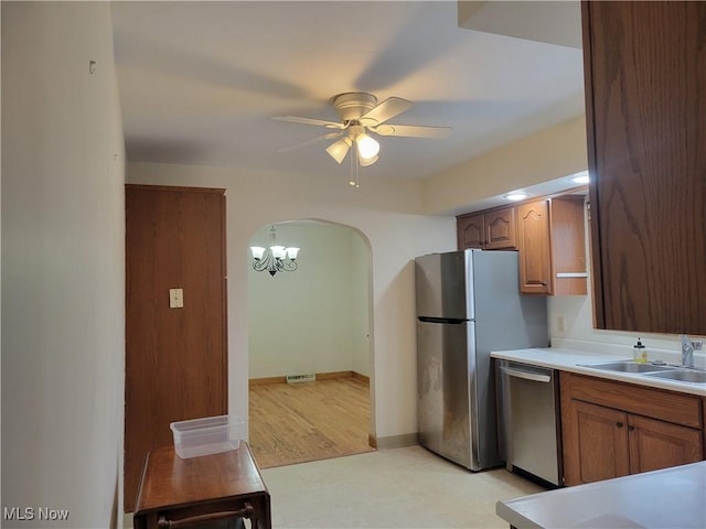 kitchen with arched walkways, brown cabinets, stainless steel appliances, light countertops, and ceiling fan