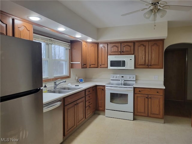 kitchen featuring arched walkways, stainless steel appliances, a sink, and brown cabinets