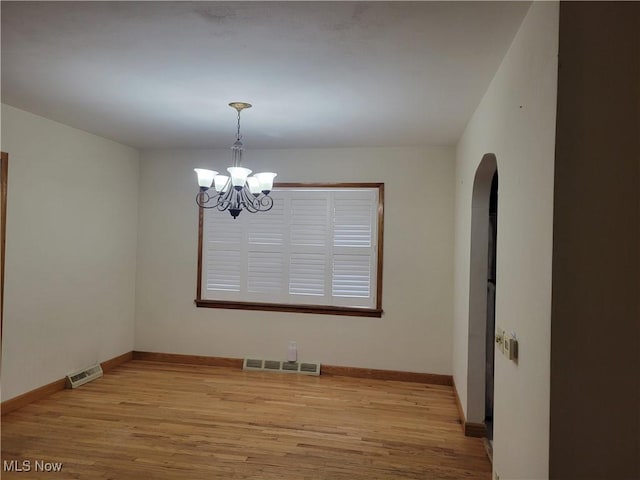 unfurnished room with wood finished floors, visible vents, and an inviting chandelier