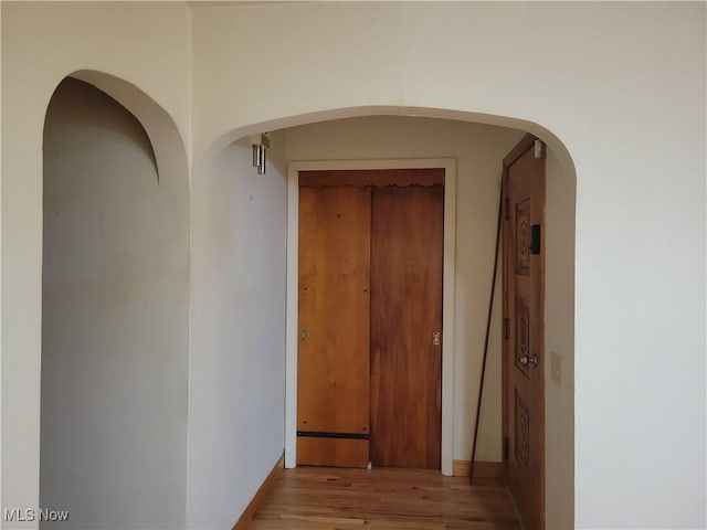 hallway with arched walkways and light wood-type flooring