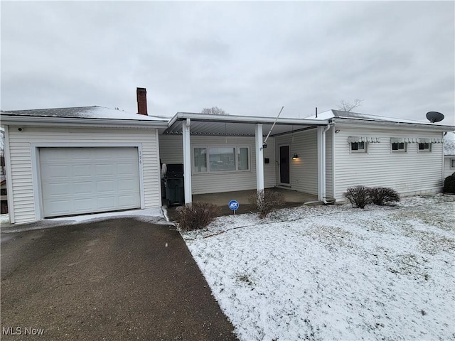 single story home with a garage, a chimney, and aphalt driveway