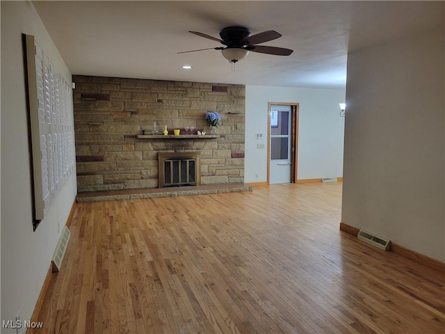 unfurnished living room featuring a stone fireplace, wood finished floors, visible vents, and baseboards