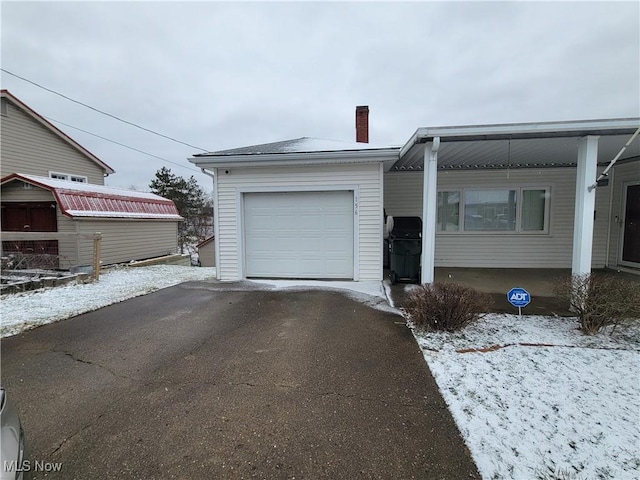 view of front of house featuring an attached garage, driveway, a chimney, and an outdoor structure