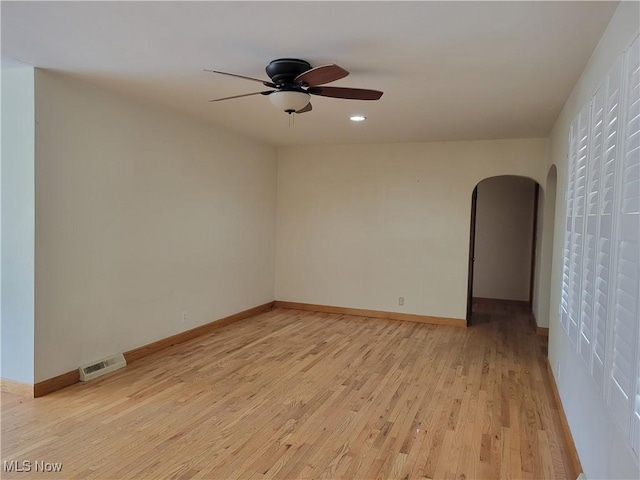 unfurnished room with visible vents, arched walkways, a ceiling fan, baseboards, and light wood-style flooring