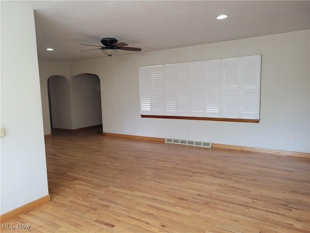 spare room with baseboards, visible vents, arched walkways, a ceiling fan, and light wood-style floors