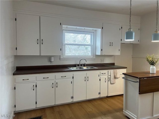 kitchen featuring wooden counters, decorative light fixtures, wood finished floors, white cabinets, and a sink