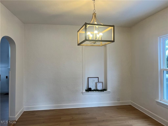 empty room with baseboards, arched walkways, wood finished floors, and a chandelier