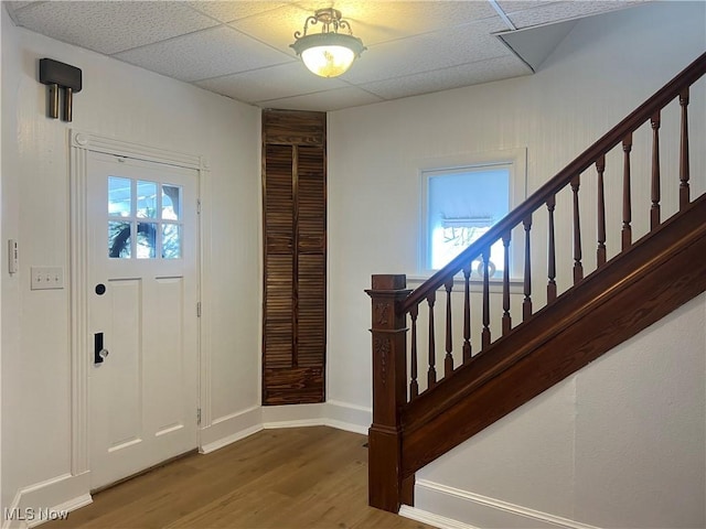 entrance foyer with stairway, a drop ceiling, baseboards, and wood finished floors