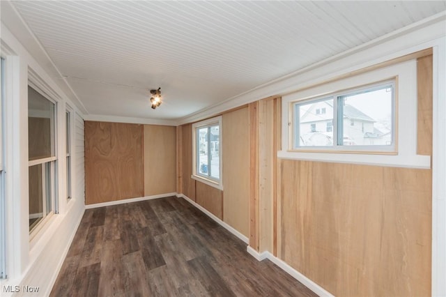 spare room featuring baseboards, wood walls, dark wood-style flooring, and a healthy amount of sunlight