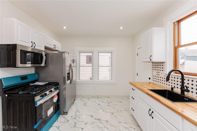 kitchen with gas range, wood counters, stainless steel microwave, marble finish floor, and a sink